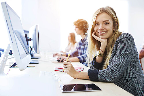 Mehrere fröhliche Personen sitzen vor iMac-Computern in einem Schulungsraum.