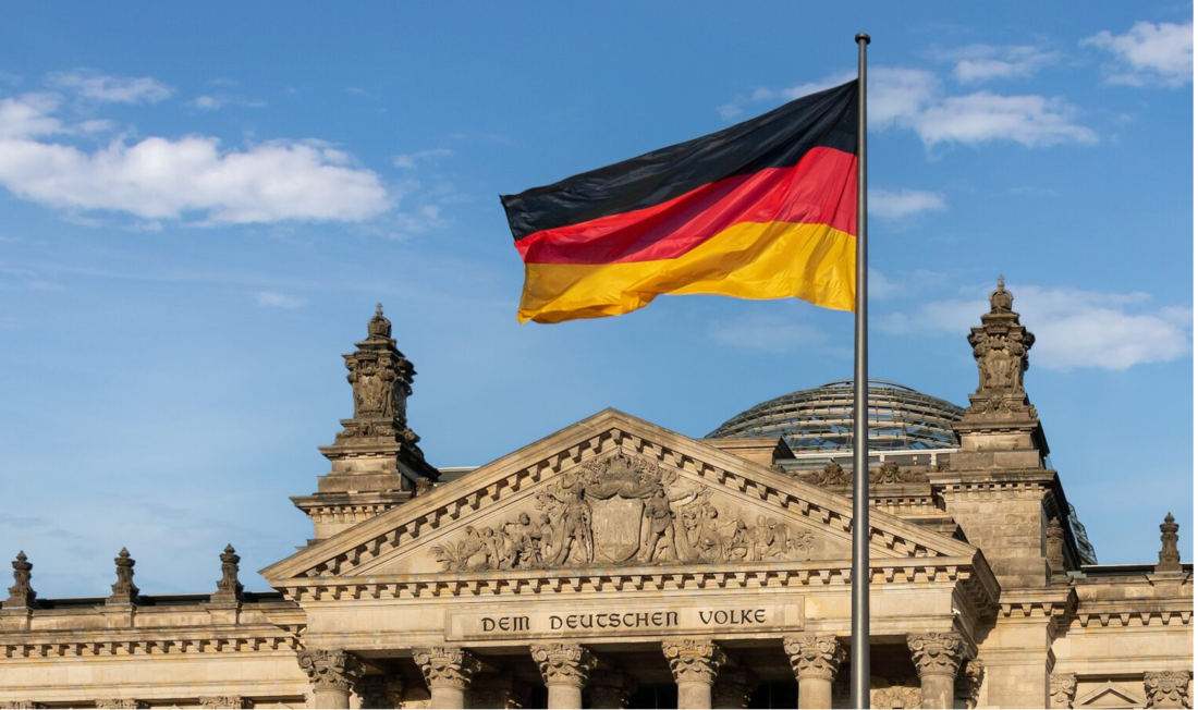 Die Vorderansicht des deutschen Bundestagsgebäudes mit wehender Deutschlandfahne im Vordergrund.