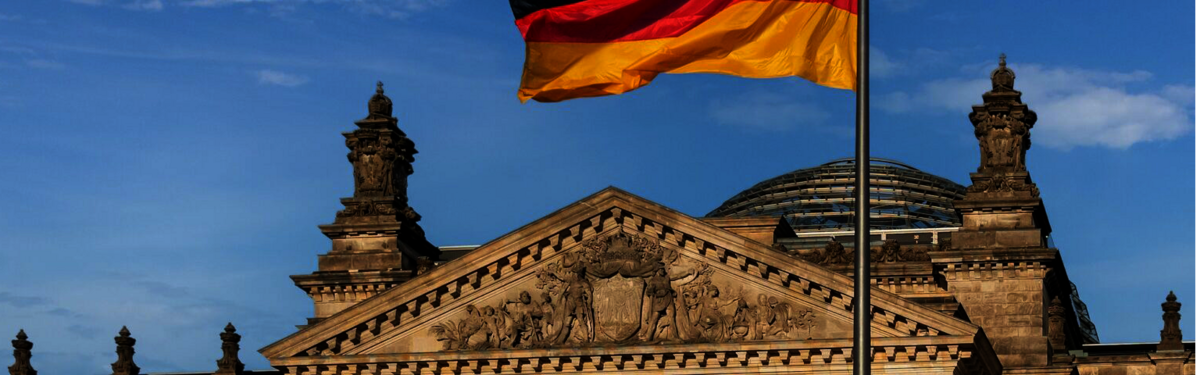 Die Vorderansicht des deutschen Bundestagsgebäudes mit wehender Deutschlandfahne im Vordergrund.