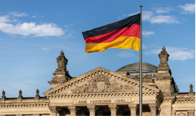 Die Vorderansicht des deutschen Bundestagsgebäudes mit wehender Deutschlandfahne im Vordergrund.