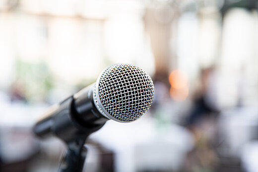 Ein Mikrofon vor einem unscharfen Hintergrund symbolisiert eine Pressekonferenz.