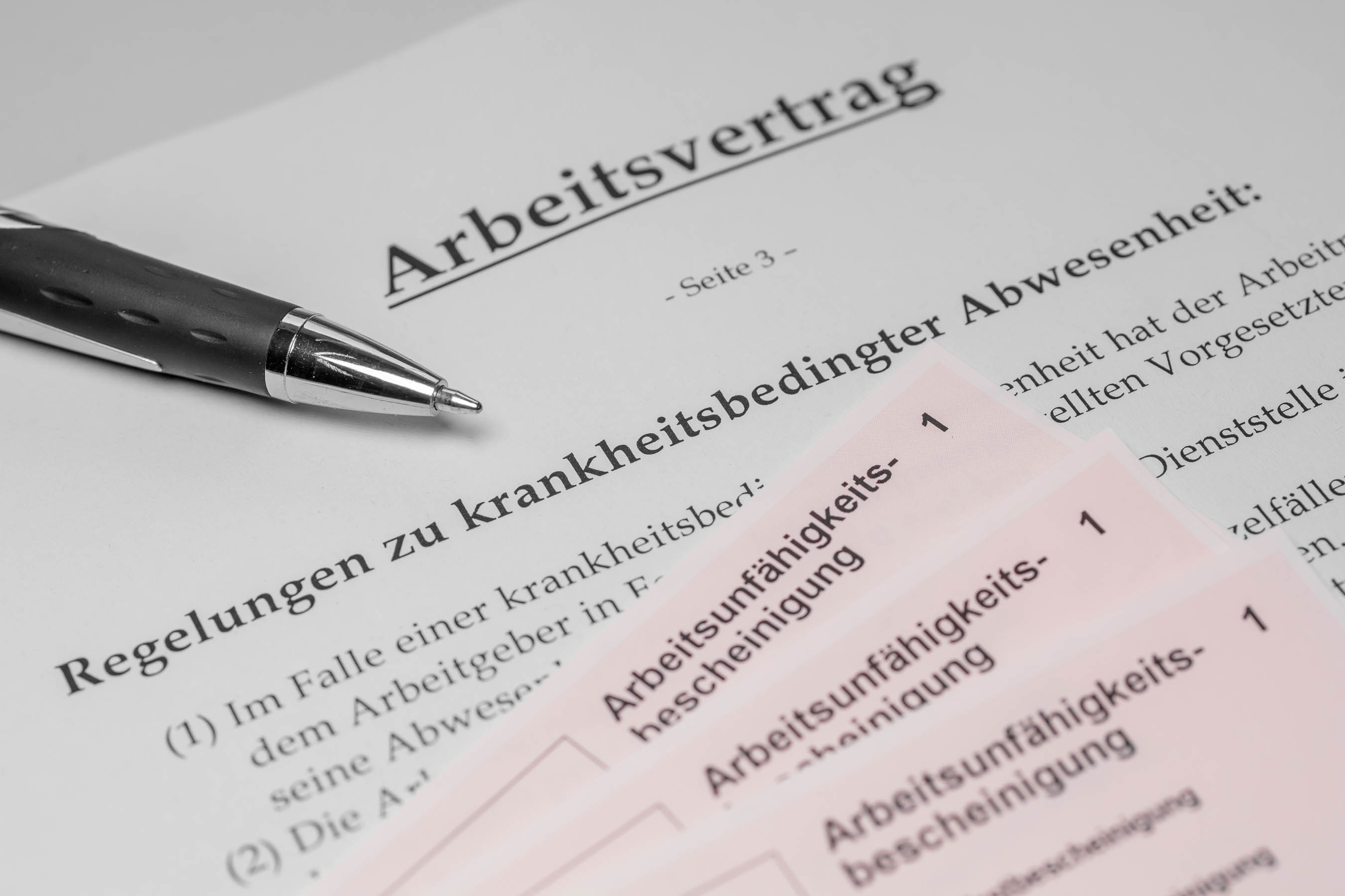 Recht-Arbeitsvertrag-001.jpg Ein Arbeitsvertrag und Krankmeldungen liegen auf einem Tisch. Darauf liegt ein Kugelschreiber.